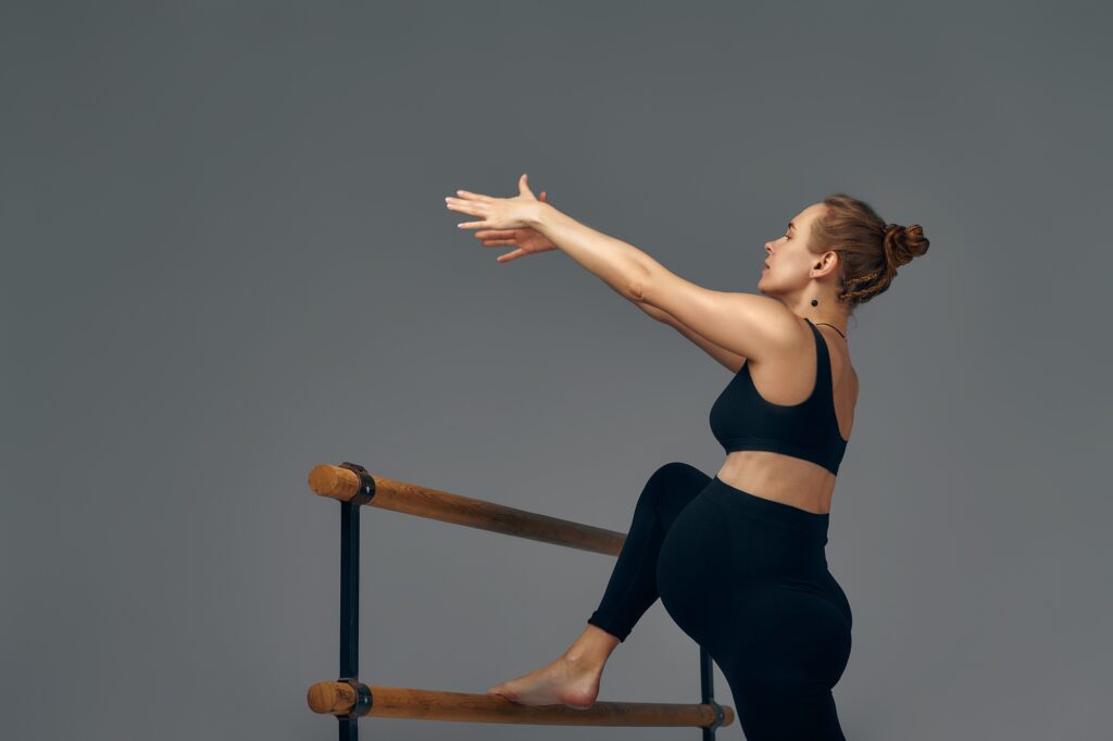 Pregnant woman posing near barre in ballet studio.