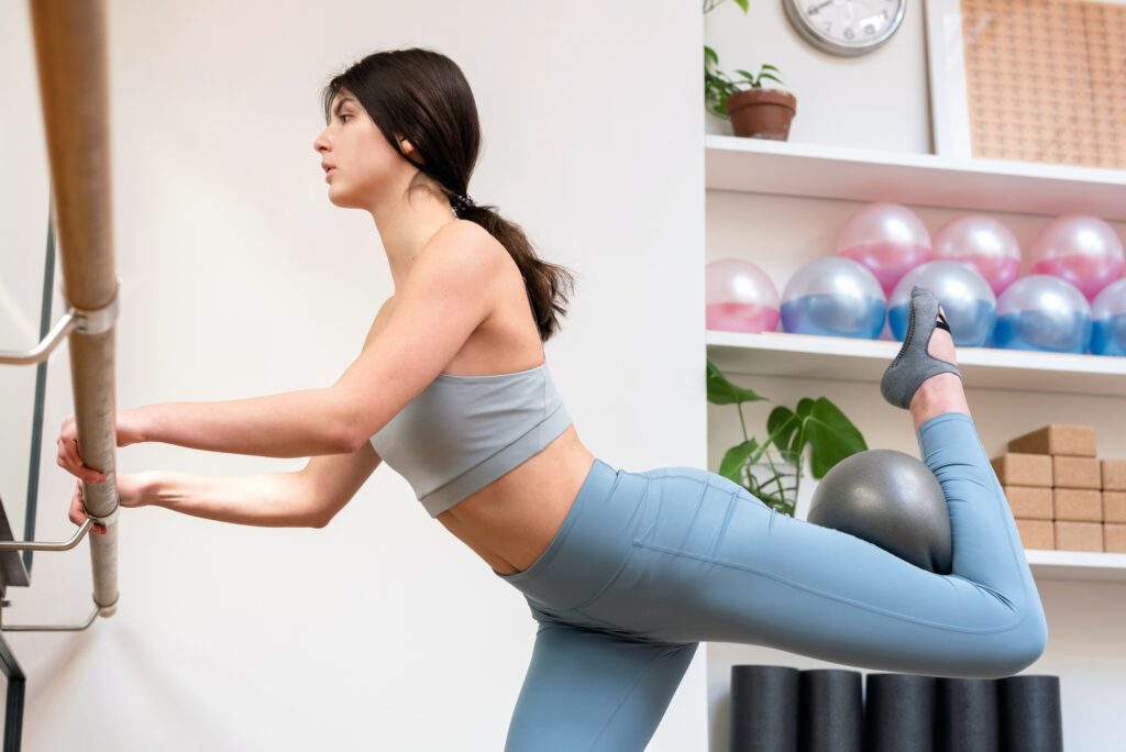 Young woman doing barre exercises with fit ball