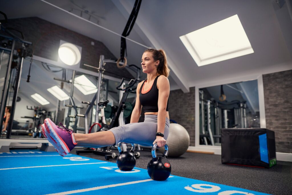 Young woman training, doing sit up push ups on kettle bells in gym